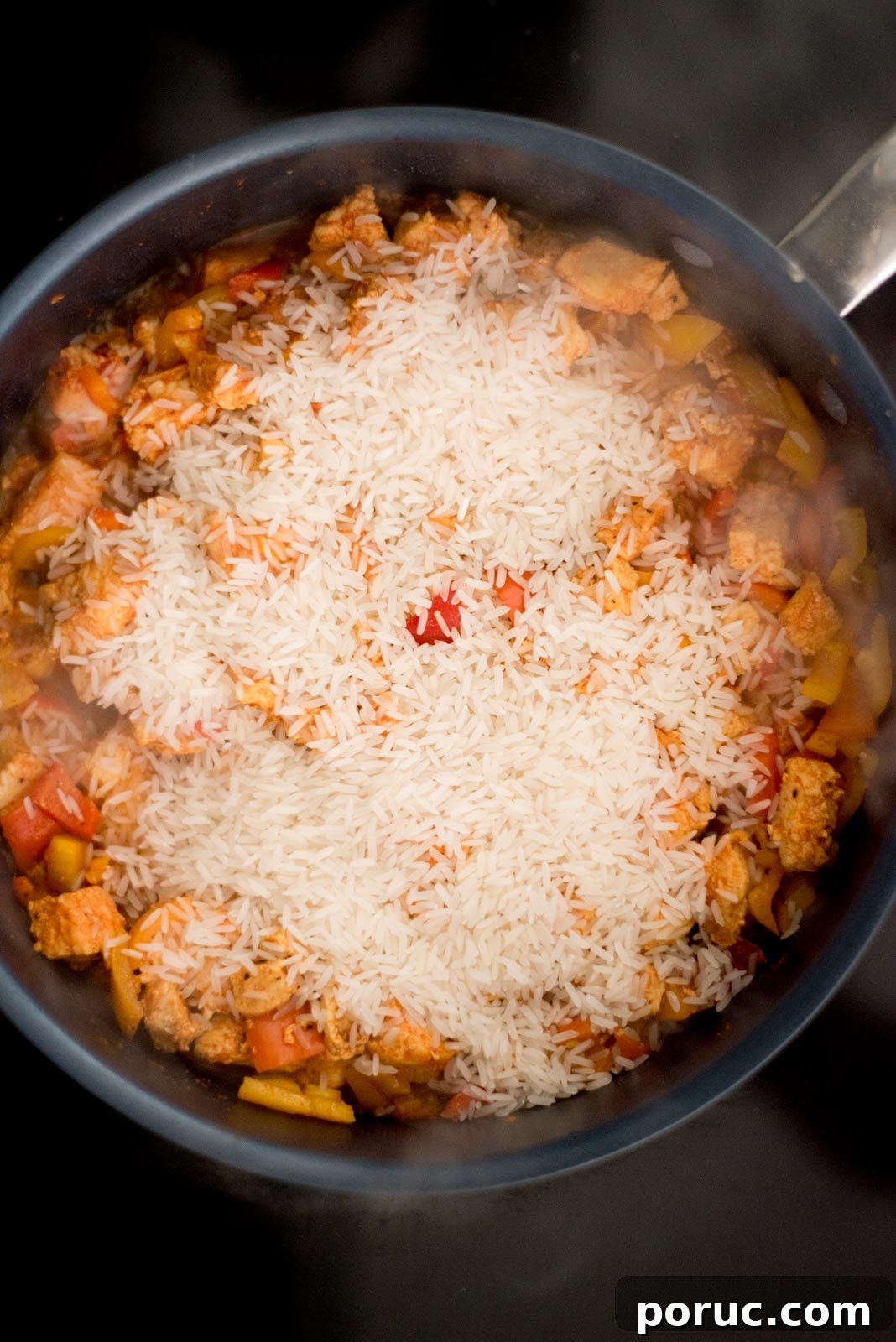 Southwest Chicken Skillet Recipe with Peppers and Black Beans 5 Rice added to the skillet on the stove with the cooked chicken and bell peppers.