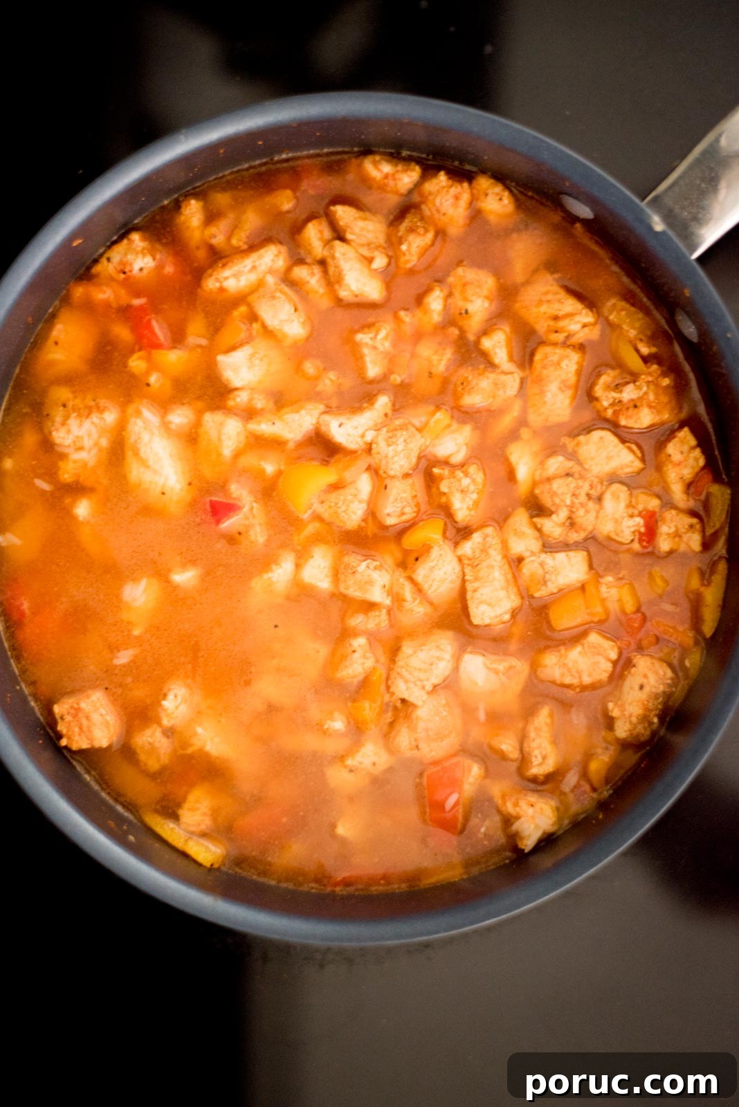 Southwest Chicken Skillet Recipe with Peppers and Black Beans 6 Liquid added to the skillet with the chicken, rice, and bell peppers on the stove.