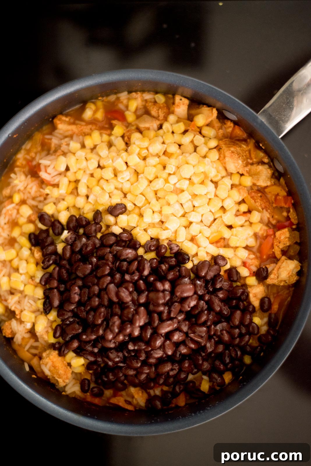 Southwest Chicken Skillet Recipe with Peppers and Black Beans 8 Corn and black beans added to the skillet with the cooked chicken, bell peppers, and rice on the stove.