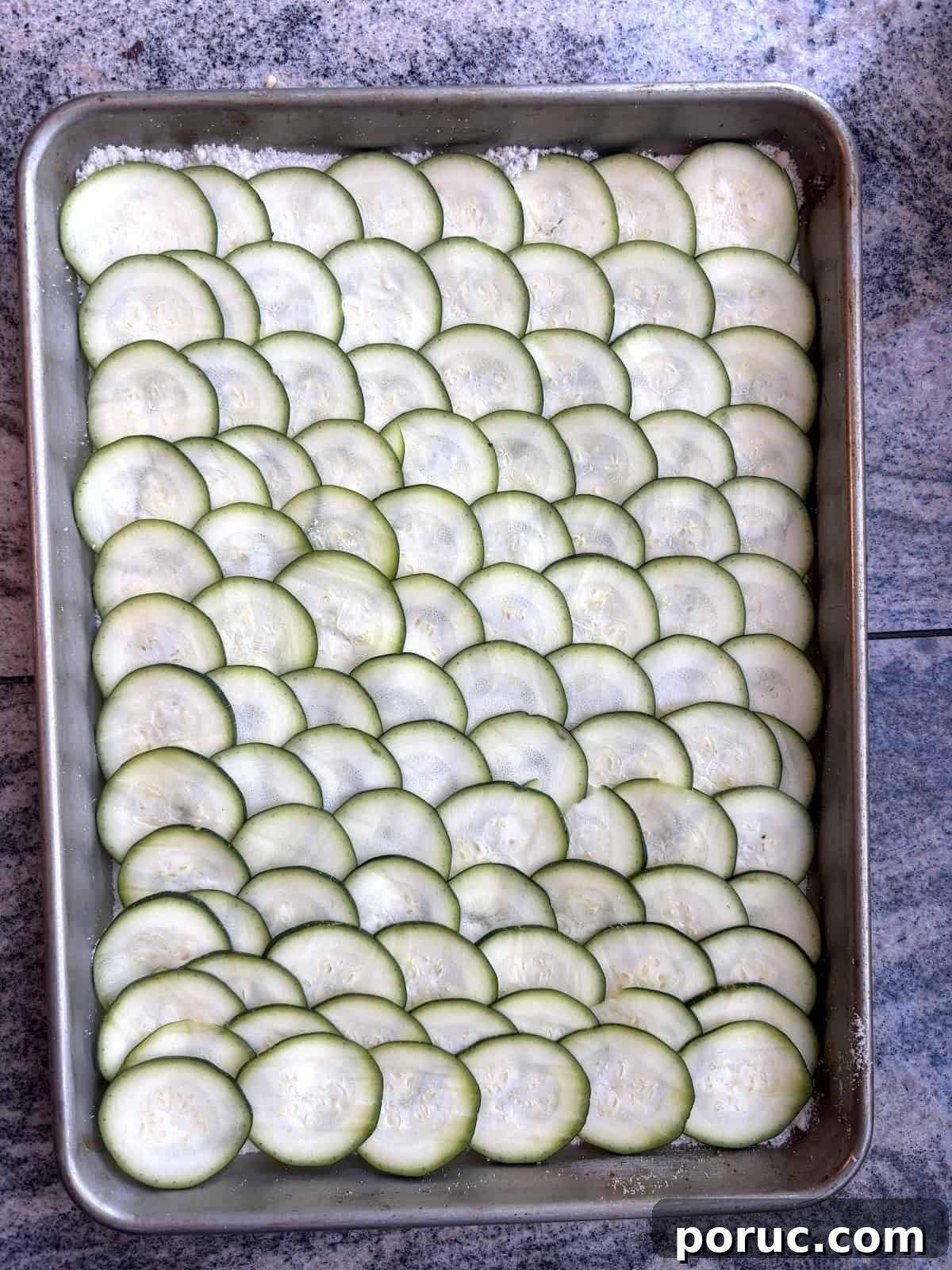 Crispy Parmesan Baked Zucchini Slices 4 A baking sheet with thinly sliced zucchini that lays of top of layer of grates parmesan cheese