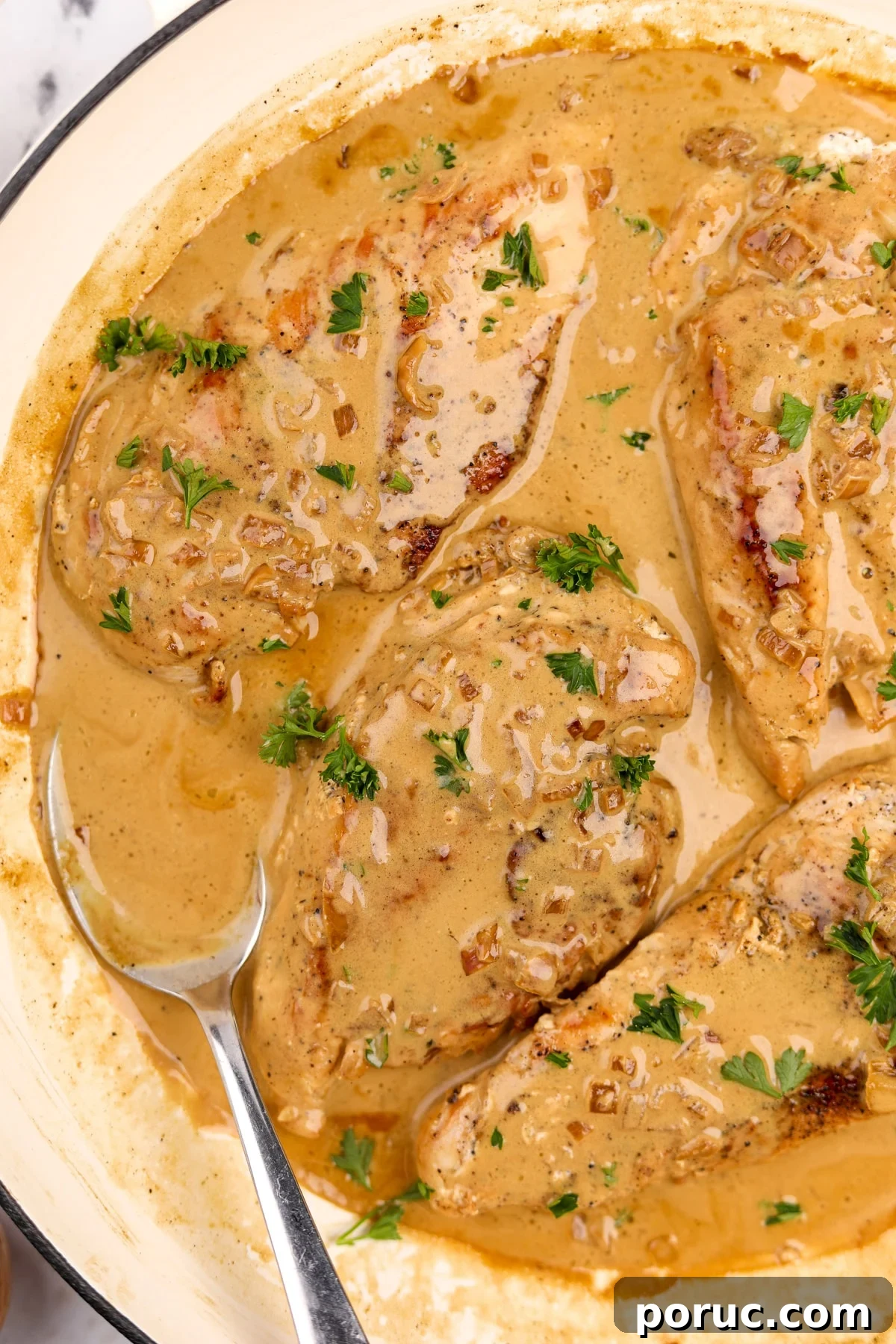 Four chicken breasts in a creamy pan sauce, with a spoon of sauce on the side.