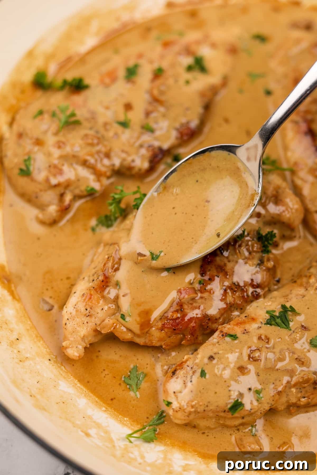Spooning sauce on top of cooked chicken breasts.