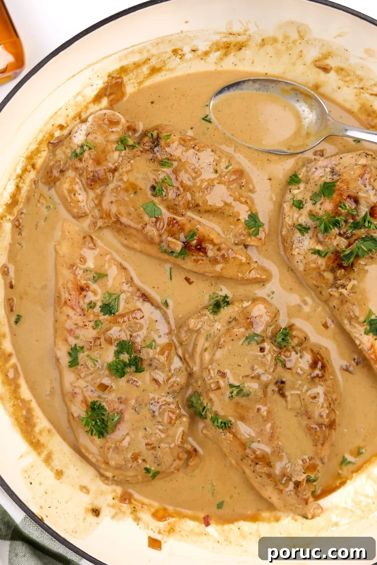 A skillet with chicken breasts covered in a creamy sauce.
