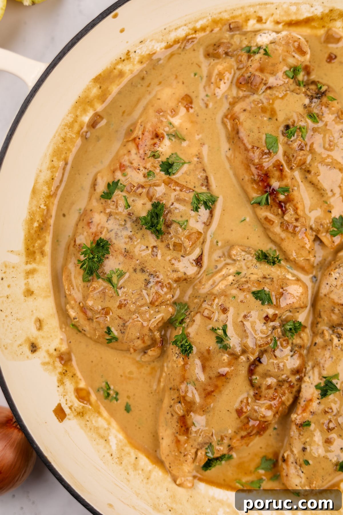 A coated cast iron skillet with creamy chicken breasts garnished with parsley.