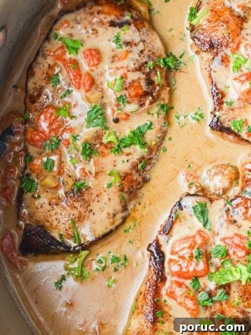 A skillet filled with chicken breasts coated in a red pepper cream sauce, and garnished with parsley.