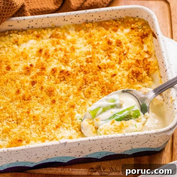 Close up view of asparagus casserole in white baking dish, with a spoon scooping out some asparagus.