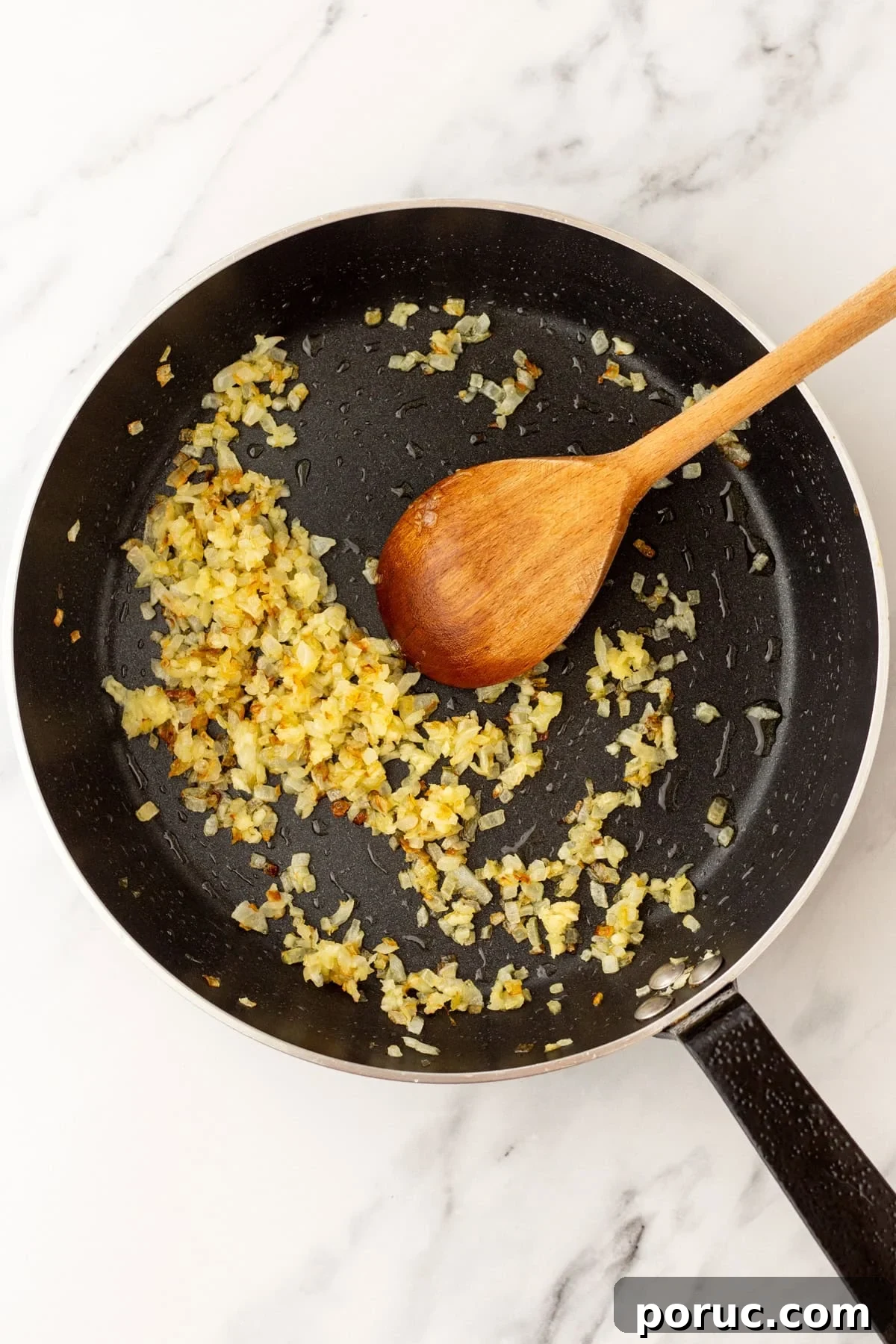An overhead image of sauteing onions and garlic on a skillet.