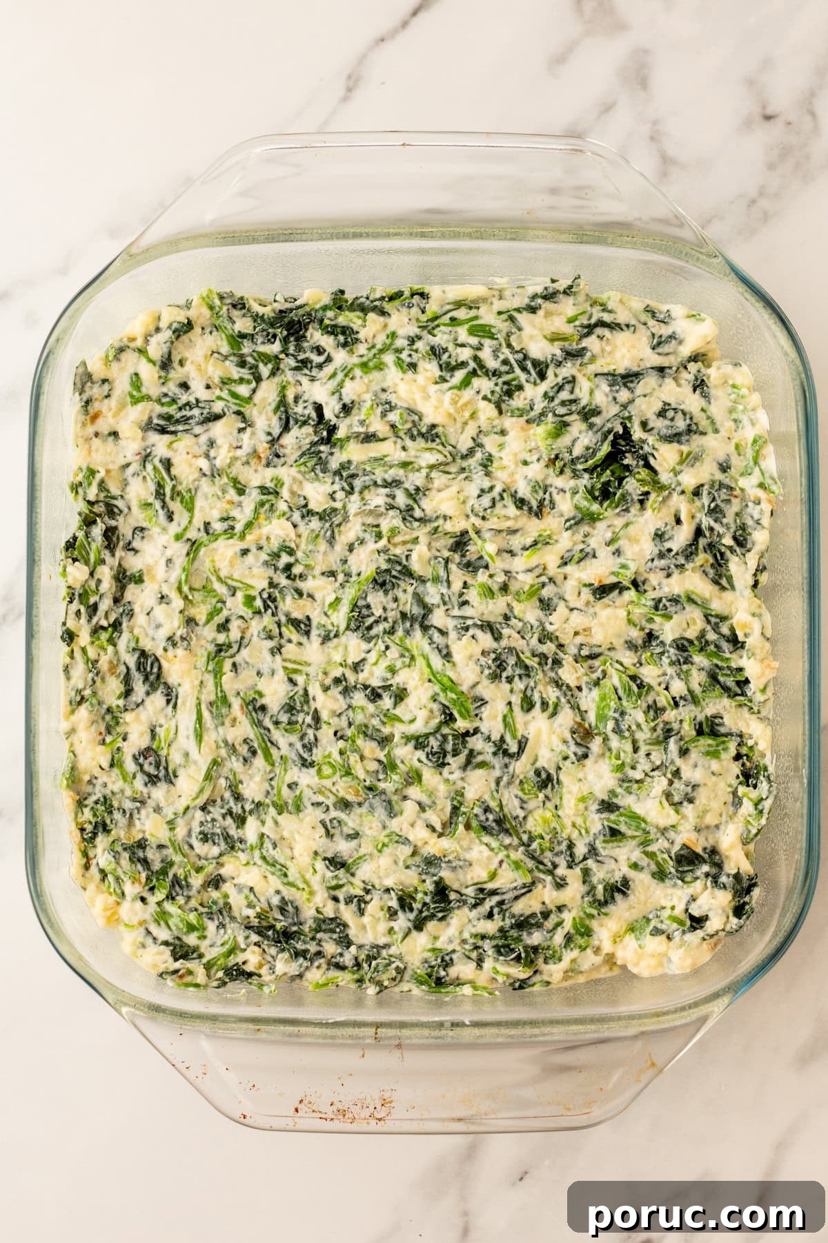 An overhead image of transferring the spinach casserole mixture in a baking dish.