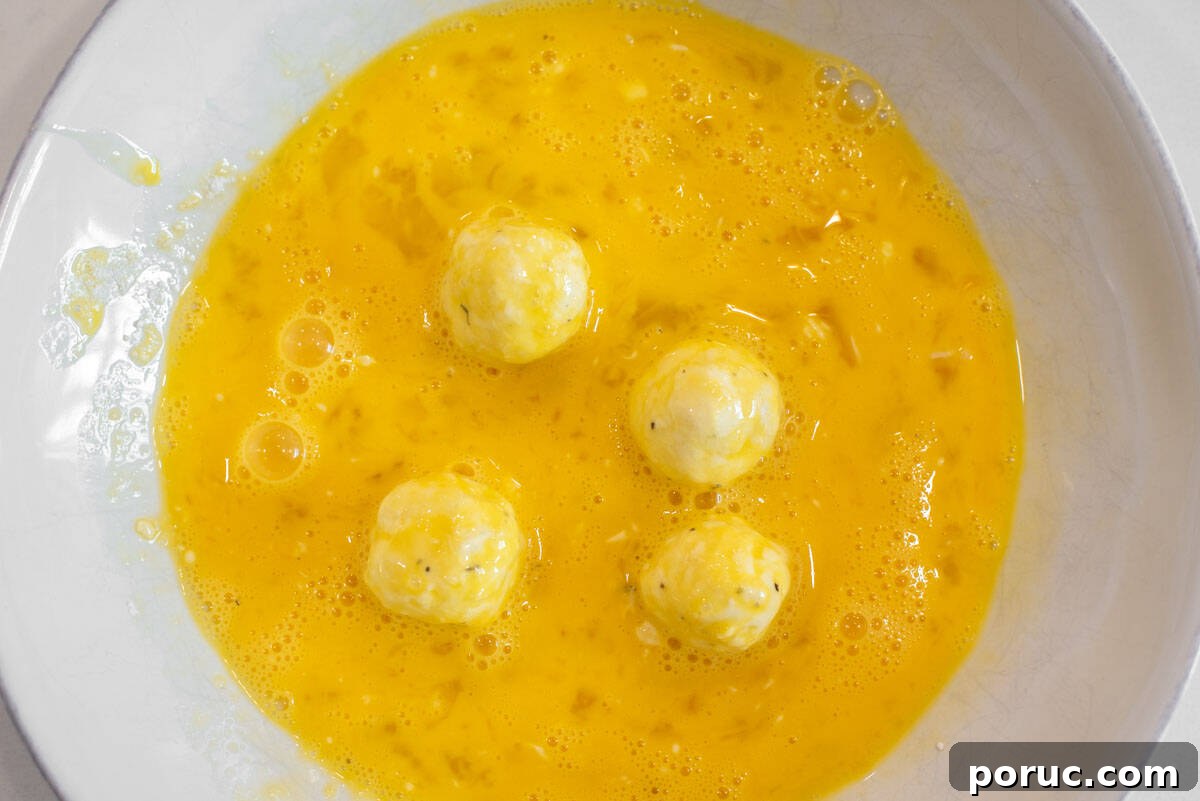 Crispy Fried Goat Cheese Balls with Honey Dip 6 Goat cheese balls dipped in eggs in bowl.