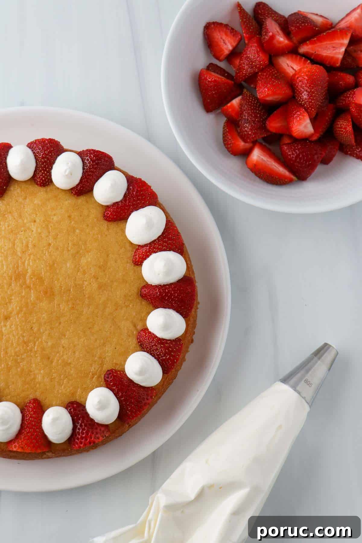 Vanilla Layer Cake with Strawberry Filling — Swedish Midsummer Cake 14 Cake with a whipped cream and strawberry border next to a bowl of strawberries an a pastry bag filled with whipped cream.
