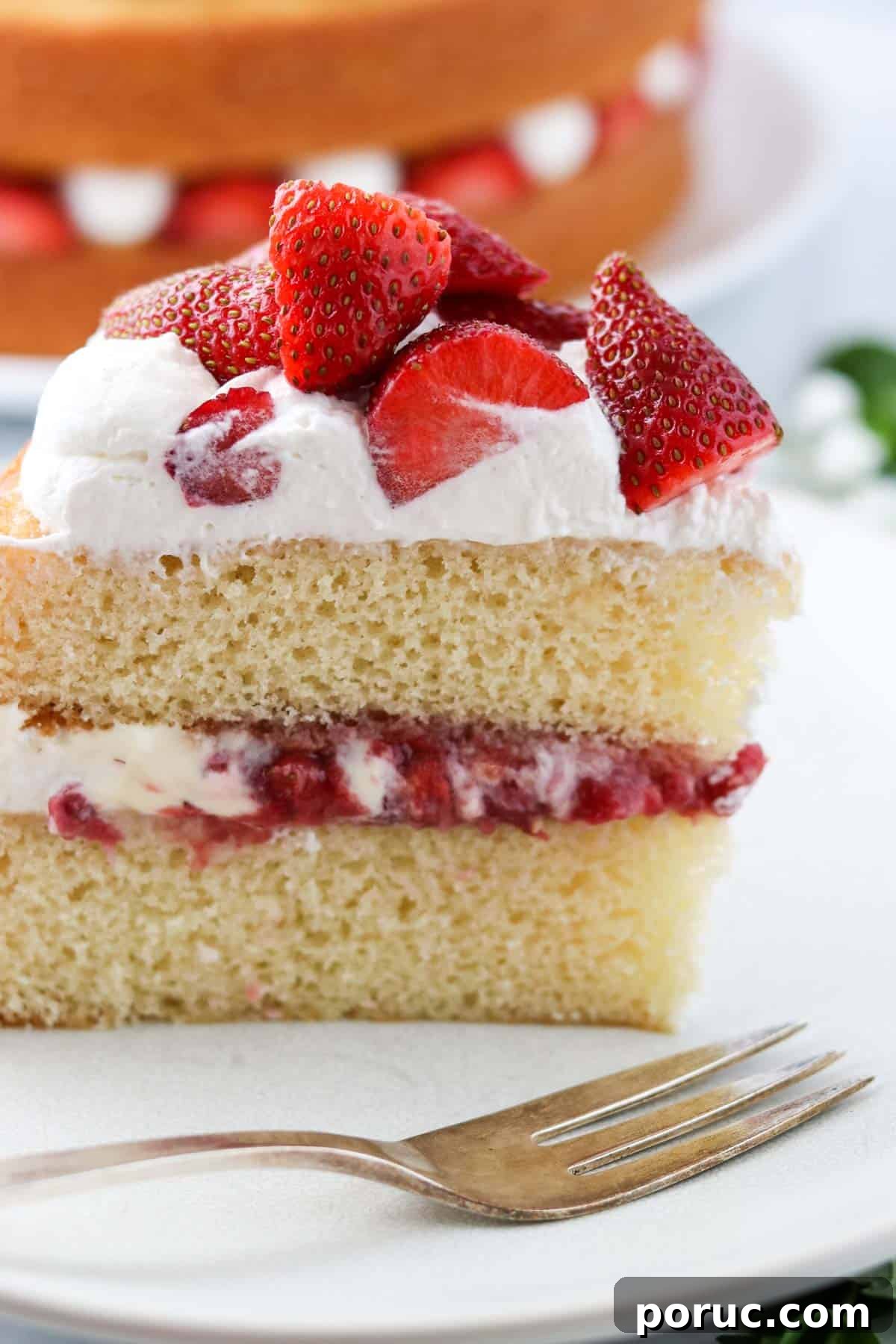 Vanilla Layer Cake with Strawberry Filling — Swedish Midsummer Cake 17 Upright slice of vanilla cake with strawberry filling next to a fork.