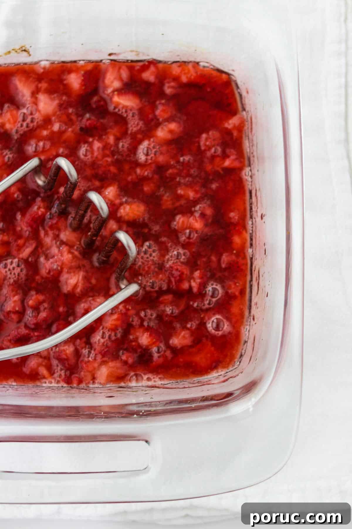 Vanilla Layer Cake with Strawberry Filling — Swedish Midsummer Cake 9 Mashed roasted strawberries in a glass dish with a potato masher.