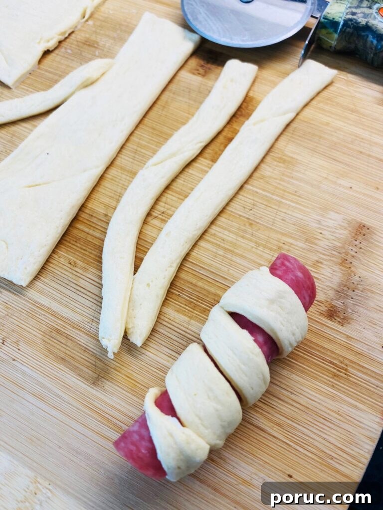 Savory Crescent Salami Roll-Ups for Appetizers and Parties 5 rolling a strip of crescent dough in a spiral around salami roll