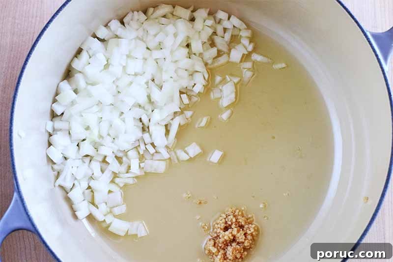 Creamy Tomato Basil Bisque That Elevates Classic Comfort Food 12 Oil, chopped white onion, and minced garlic in a white and blue enamel stock pot.