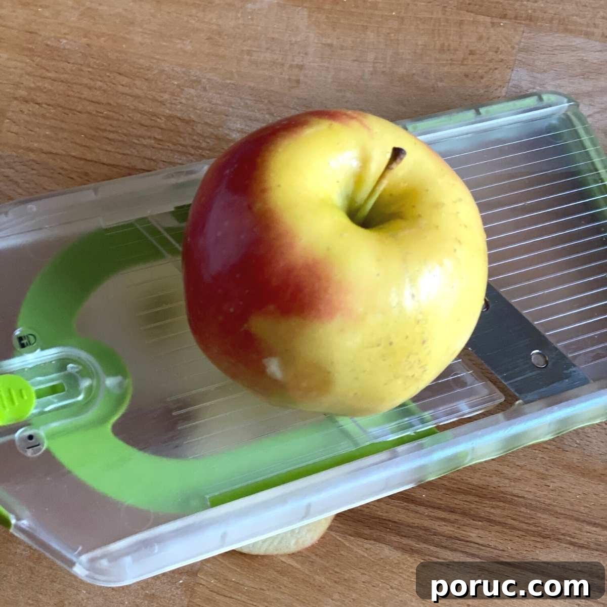 Crispy Oven-Dried Apple Chips Recipe for Snacking 3 Apple placed on top of a mandoline slicer with the core stem showing.