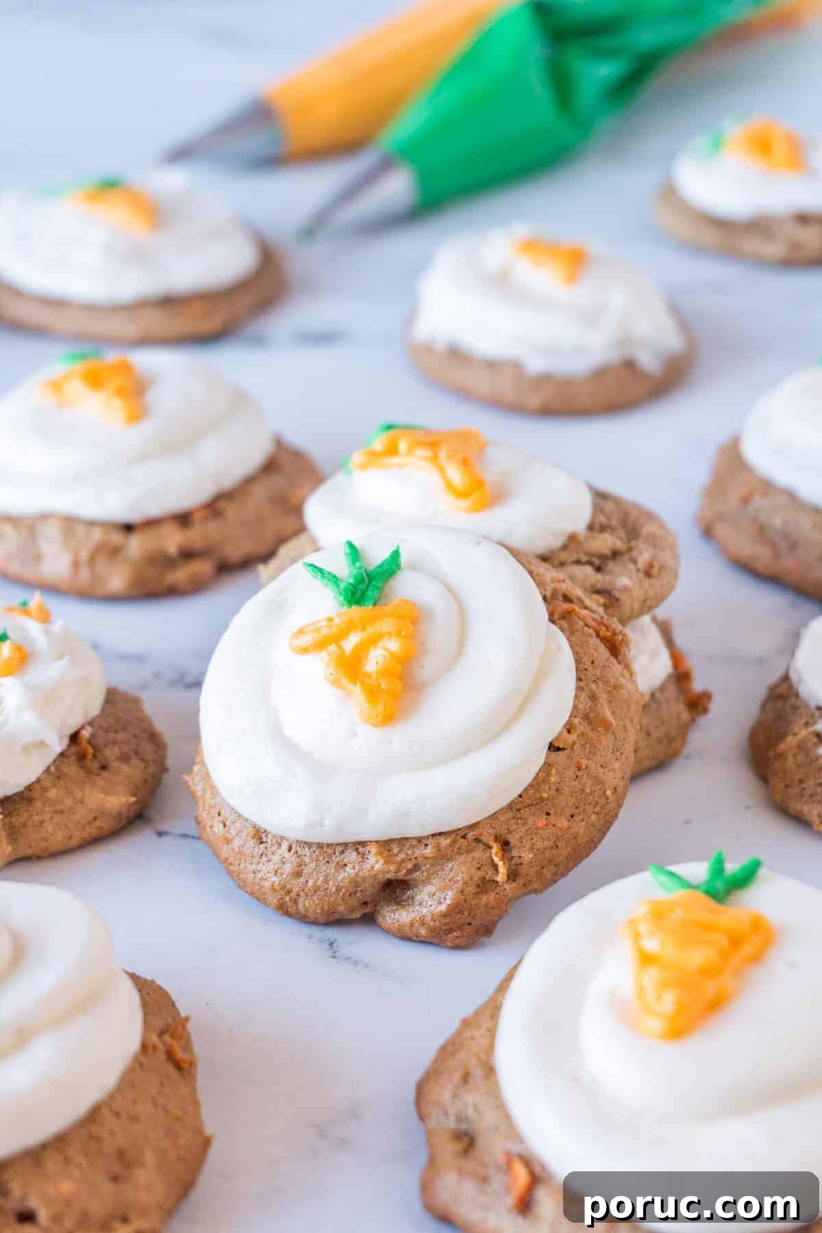 carrot cake cookies with cream cheese frosting and little carrots piped, stacked on one another, on a marble background.