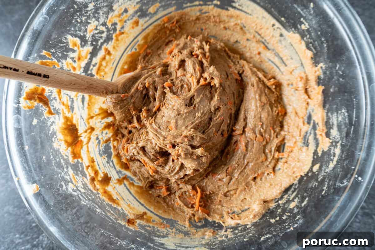 carrot cake cookie dough mixed in a glass bowl with a wooden spoon.