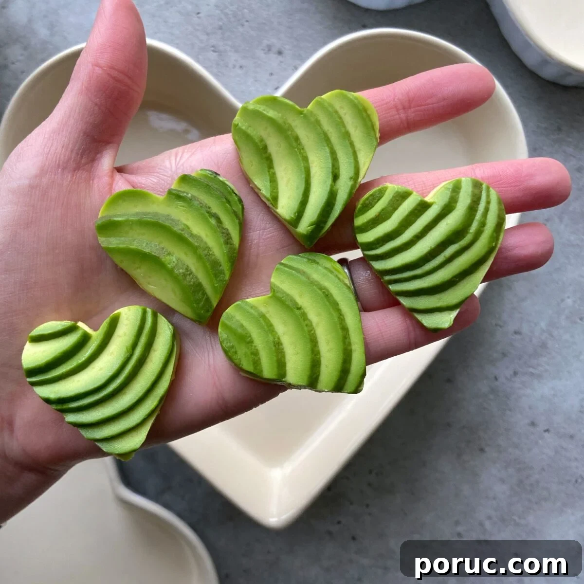Creamy Avocado & Melted Cheese Toast Recipe 3 A hand holding five heart-shaped avocado slices.