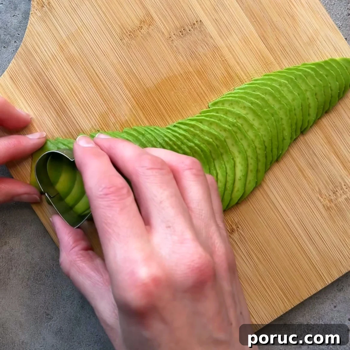 Creamy Avocado & Melted Cheese Toast Recipe 4 A person uses a heart cookie cutter mold to shape thinly sliced avocado.