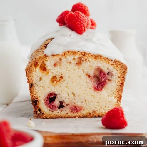 A raspberry loaf cake covered with a white glaze and fresh raspberries.