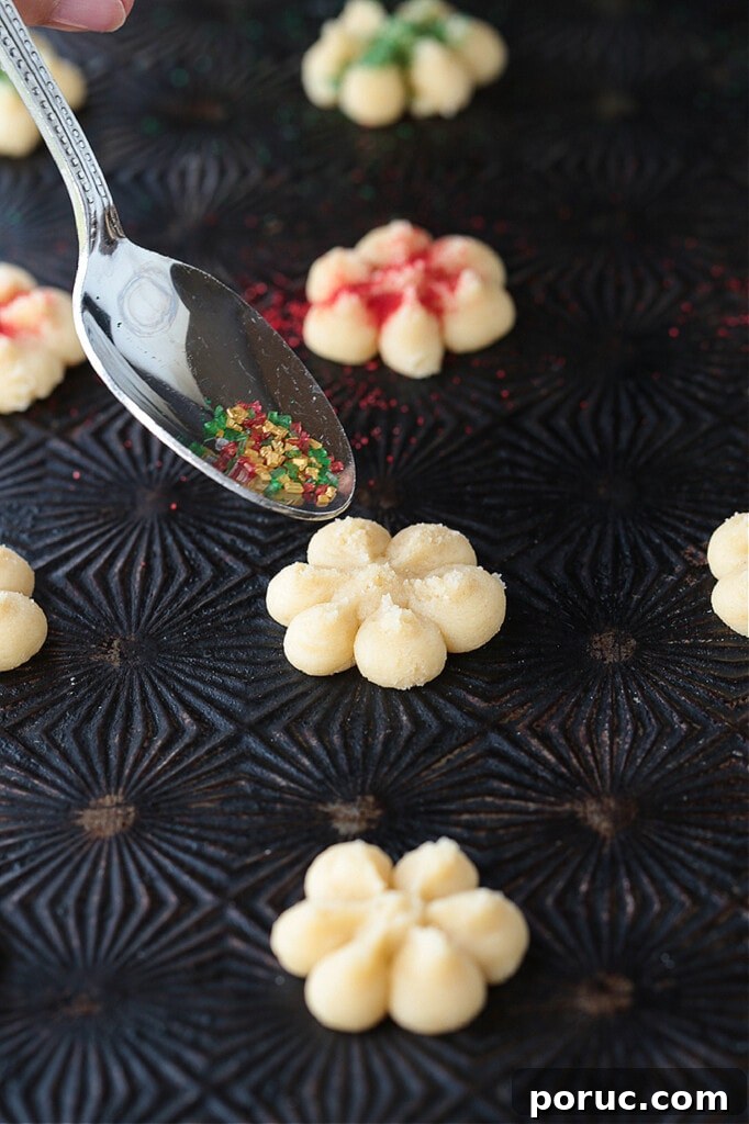 Grandma's Spritz Cookies are a family favorite! Buttery, festive cookies with a hint of sweetness, topped with colorful sprinkles. spoon with sprinkles topping a cookie
