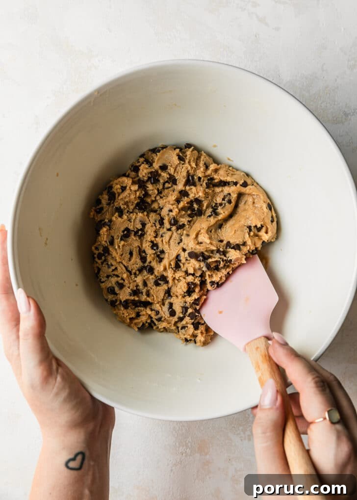 Chewy Mini Chocolate Chip Cookie Recipe for Perfect Bites 15 Hands using a pink rubber spatula to mix cookie dough in a white bowl.