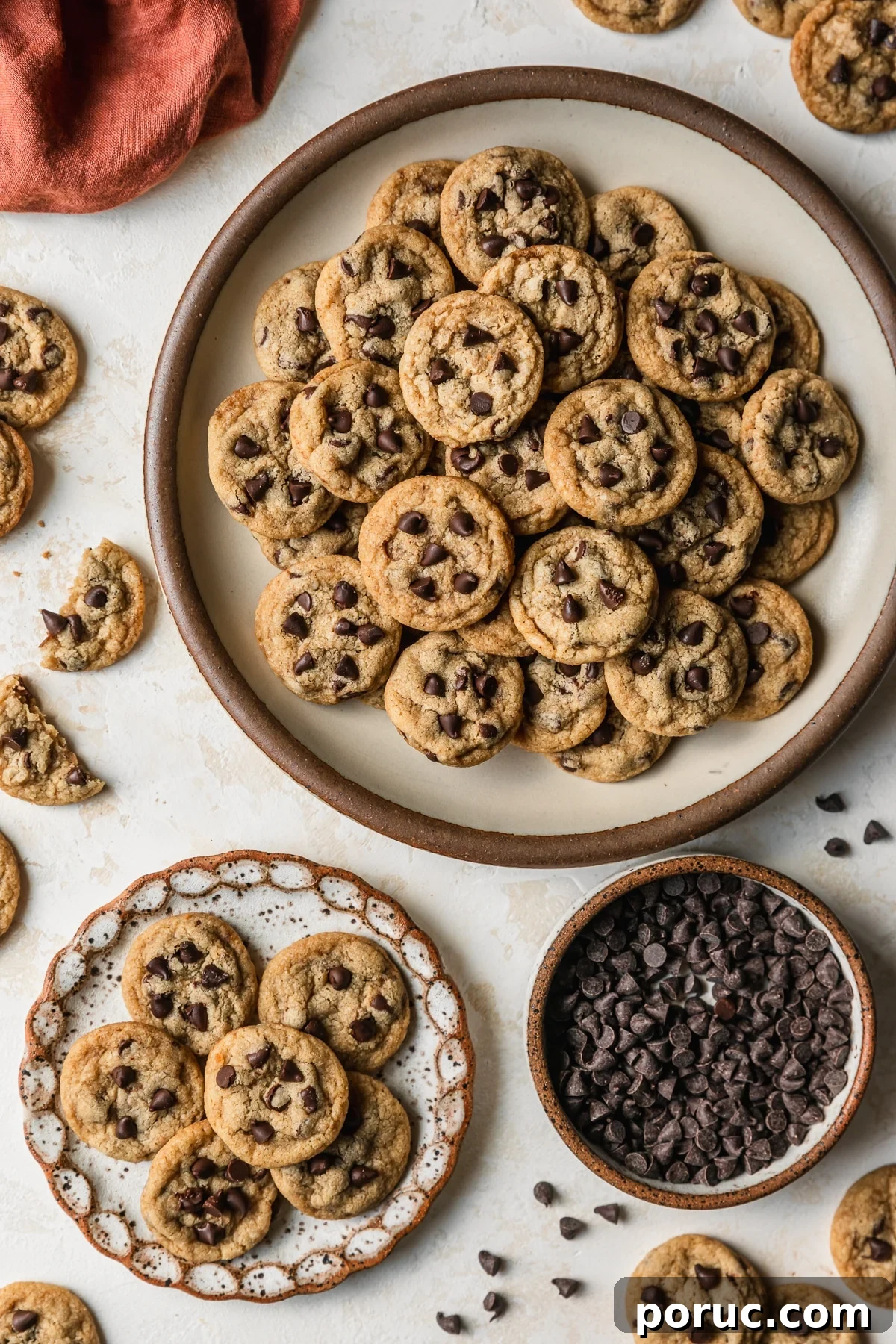 Chewy Mini Chocolate Chip Cookie Recipe for Perfect Bites 20 White and stoneware plates of mini chocolate chip cookies on a tan counter next to a brown bowl of chocolate chips, mini cookies, and an orange linen.