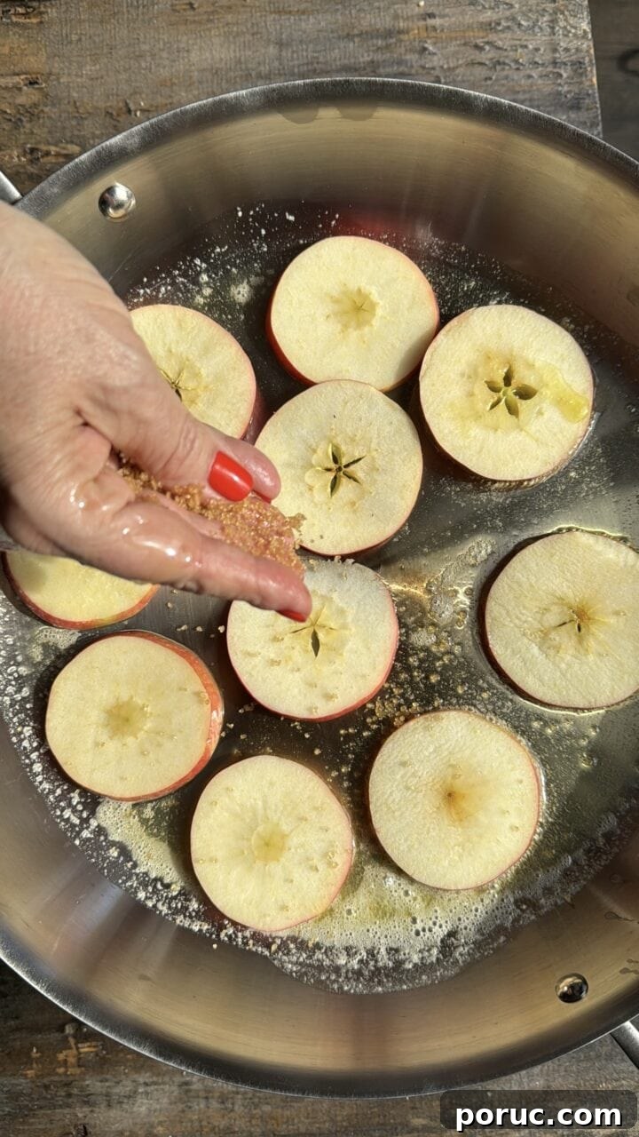 Sliced apples being seasoned in a stainless steel pan, preparing for cooking or baking.
