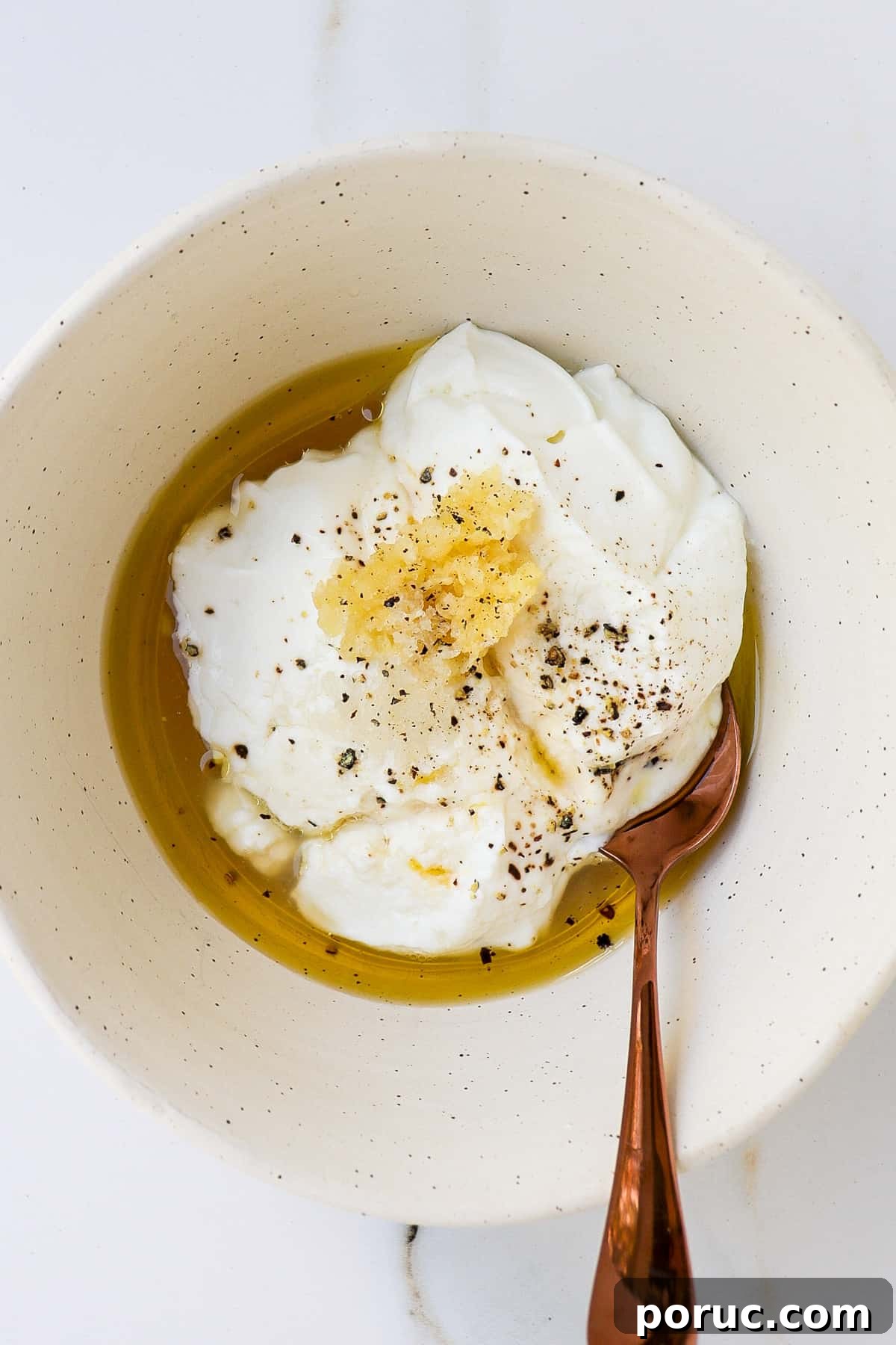 Yoghurt dressing ingredients in a white bowl with gold spoon.