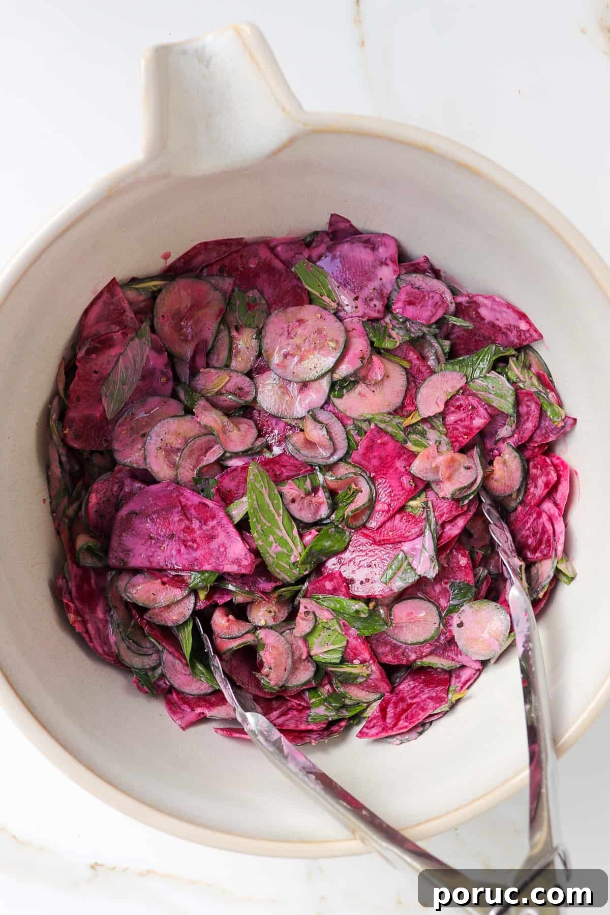 Cucumber beetroot salad in a mixing bowl with metal tongs.