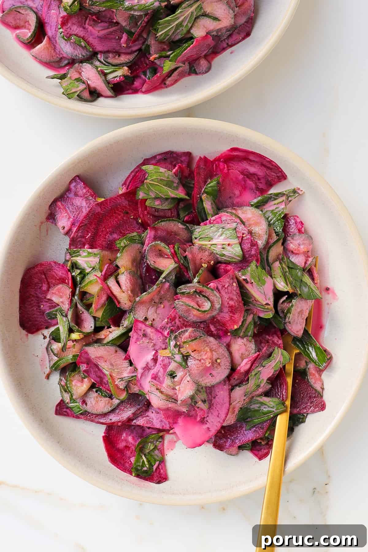Cucumber beetroot salad in bowl with gold fork.