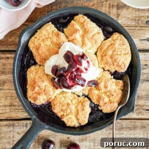 Simple Cherry Cobbler Recipe with Homemade Biscuit Topping 9 Cream topped cherry cobbler in a cast iron skillet. Wooden surface.