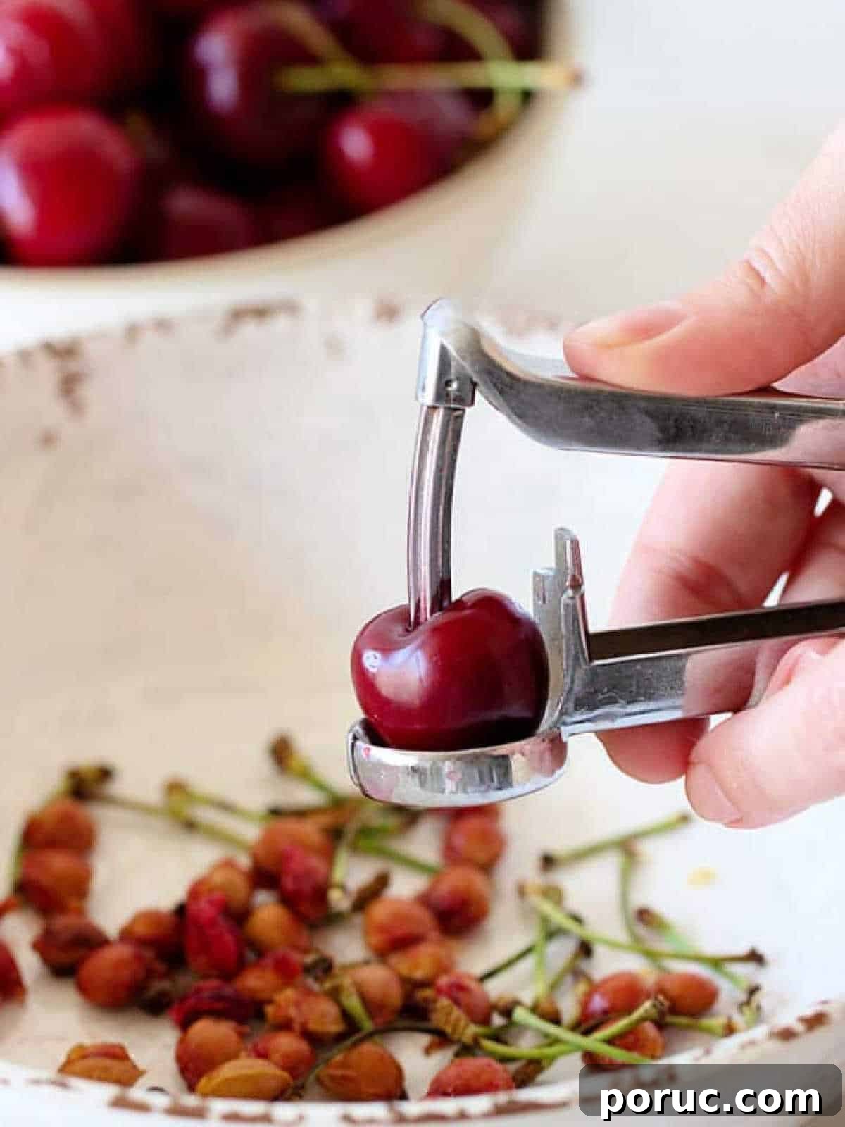 Simple Cherry Cobbler Recipe with Homemade Biscuit Topping 4 A fresh cherry being pitted over a white bowl with pits.