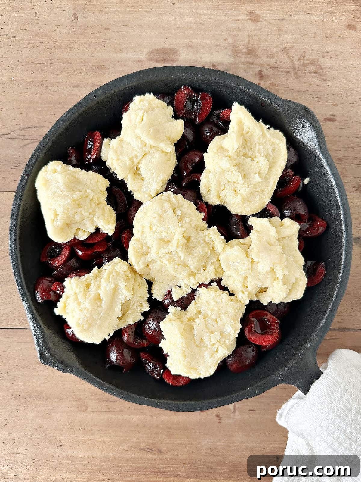 Simple Cherry Cobbler Recipe with Homemade Biscuit Topping 7 Cast iron skillet with unbaked cherry cobbler on a wooden surface.