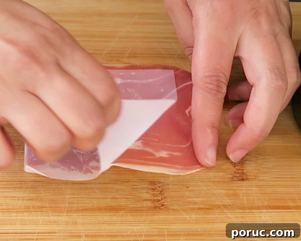 peeling the wax off a piece of prosciutto on a cutting board