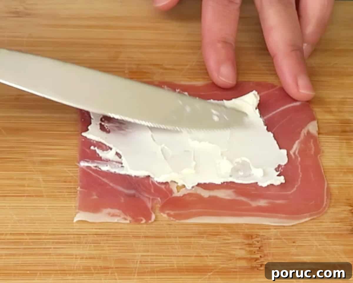 spreading cream cheese onto the prosciutto slice