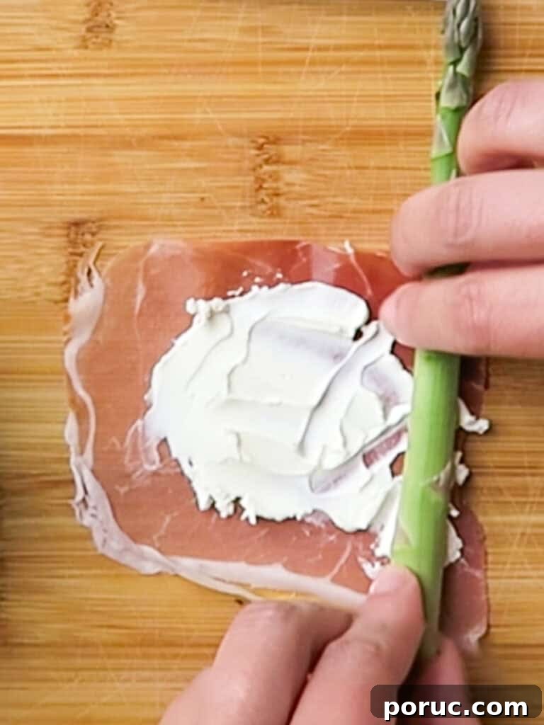 rolling the prosciutto with cream cheese around the asparagus spear