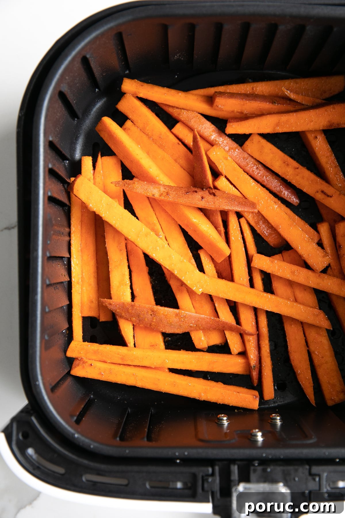 Overhead image looking into the basket of an air fryer filled with uncooked sweet potato fries.