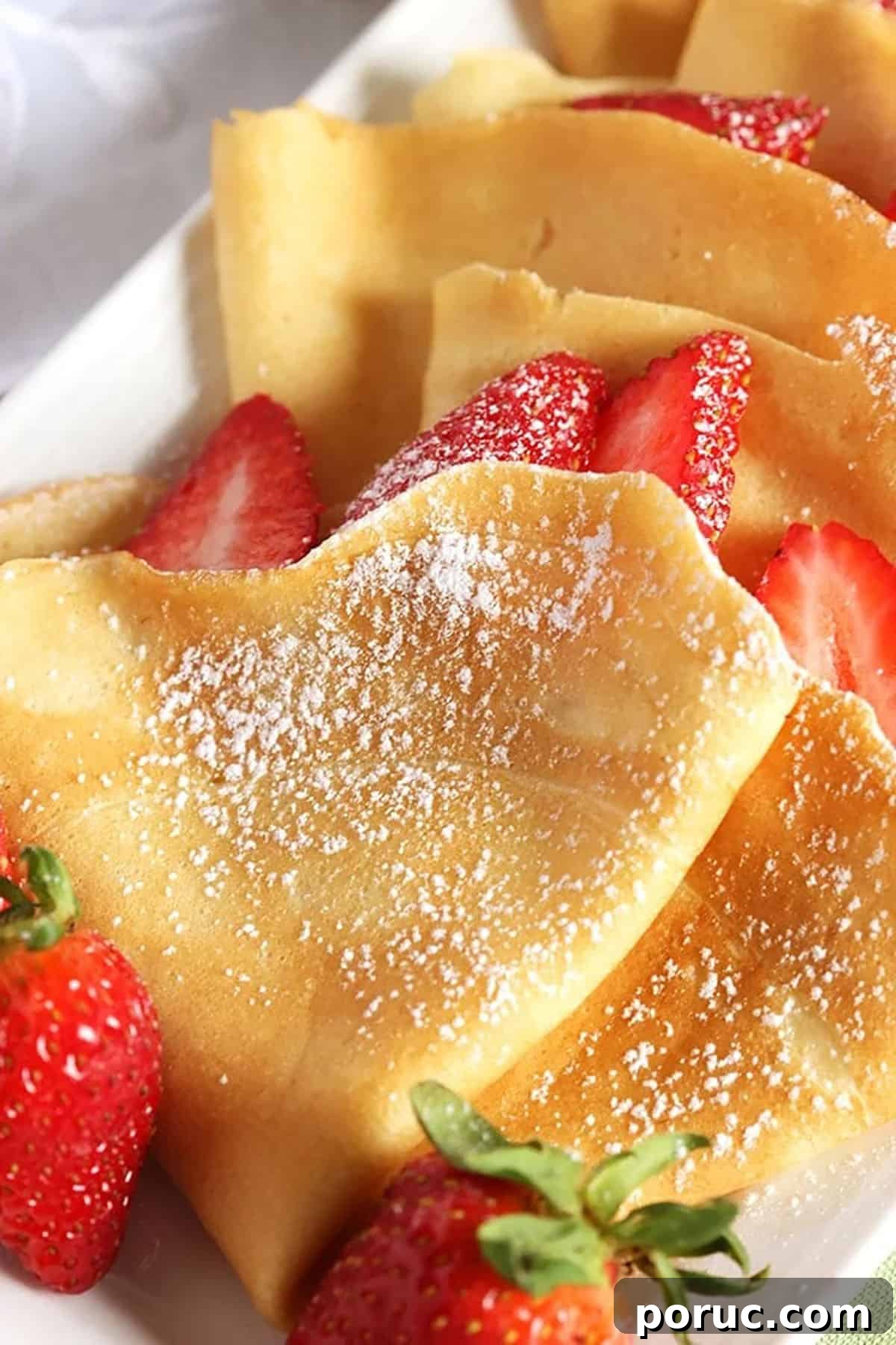Homemade Crepes: Sweet and Savory Recipes for Any Meal 4 French crepes dusted with powdered sugar on a white plate with berries