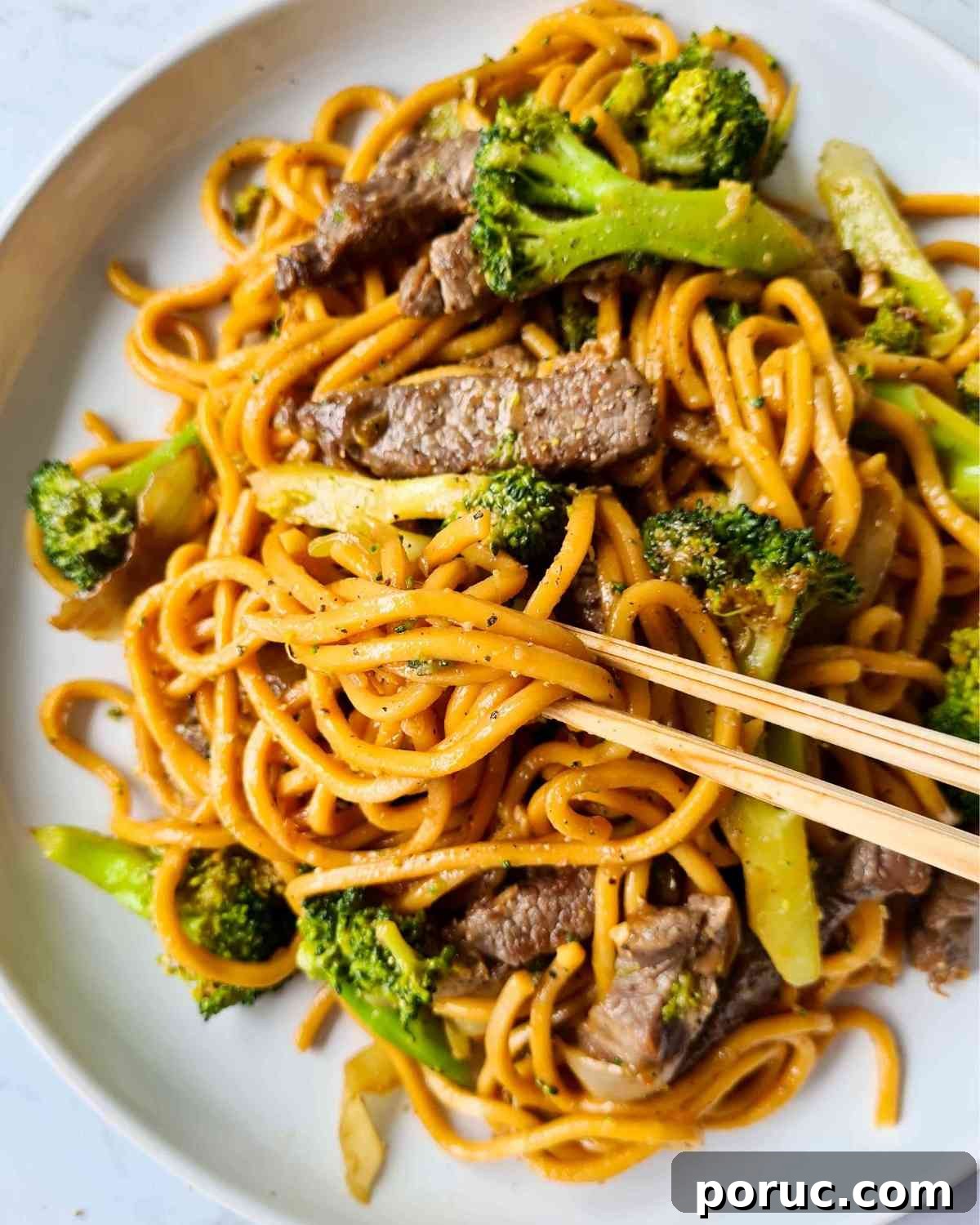 Beef and Broccoli Noodles with Garlic Soy Sauce Recipe 12 Stir fried noodles with broccoli, beef strips on a large white plate and a pair of chopsticks