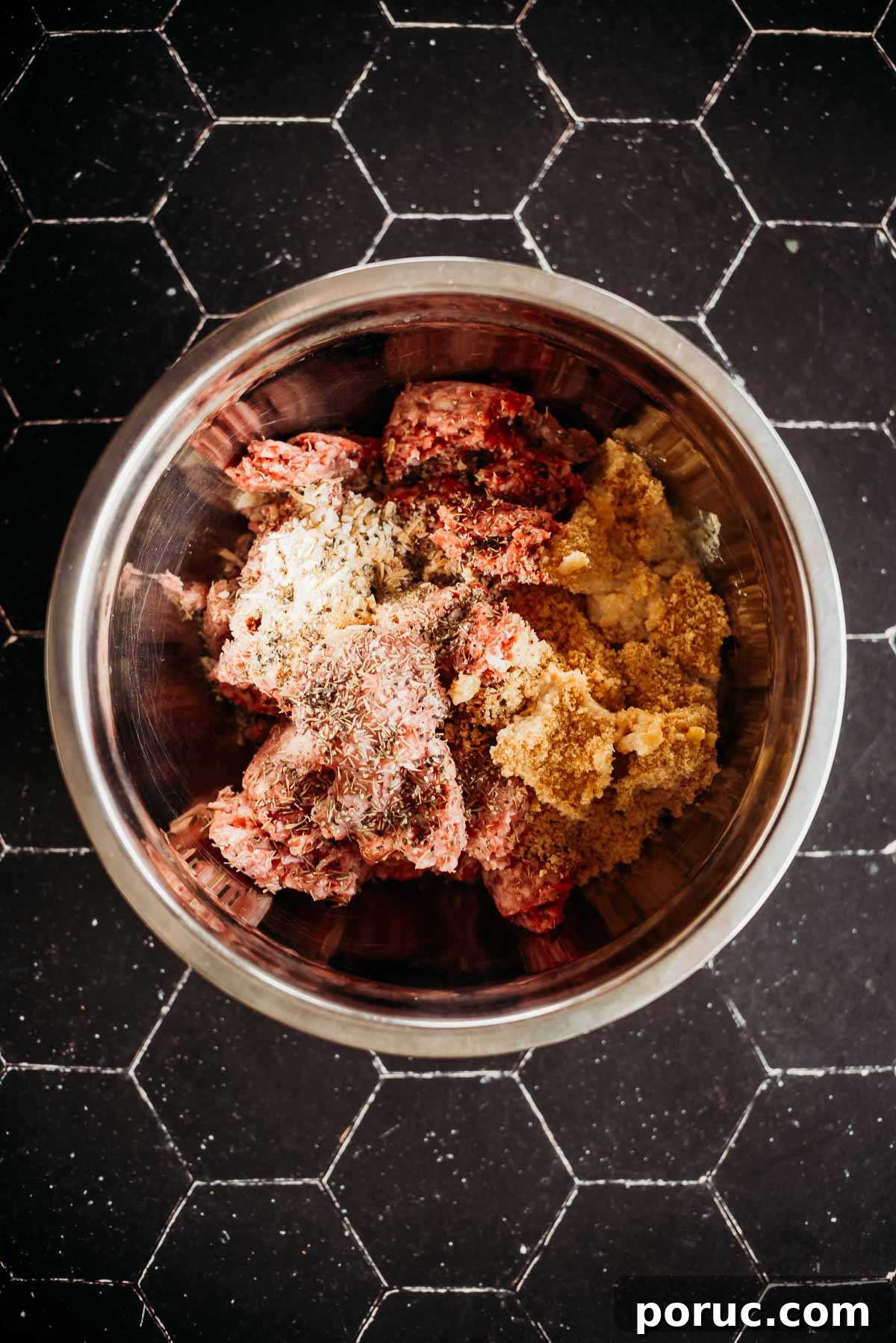 Bowl with ground meat mixed with spices and breadcrumbs on a tiled surface.