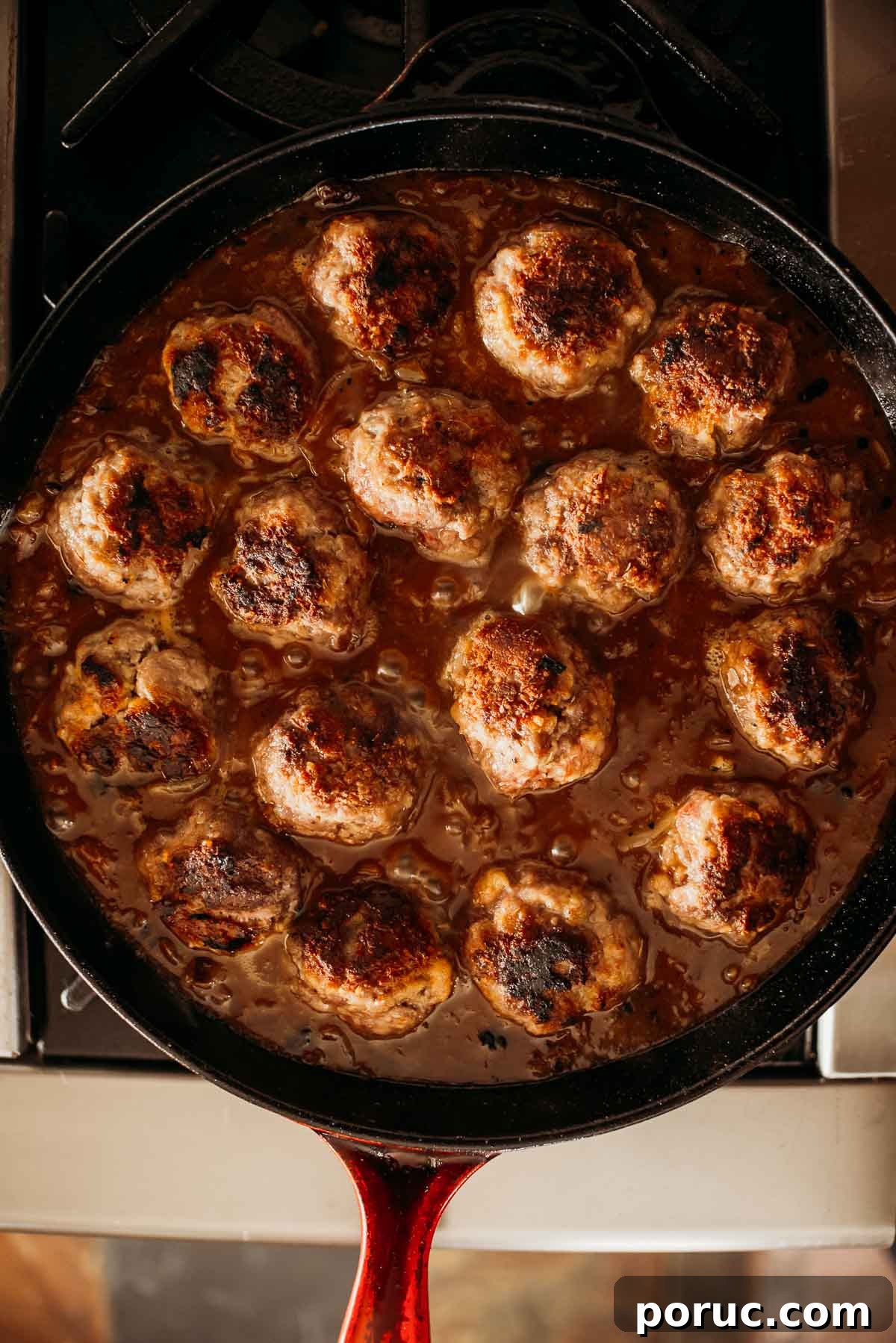 A skillet filled with evenly cooked meatballs in sauce, placed on a stove.