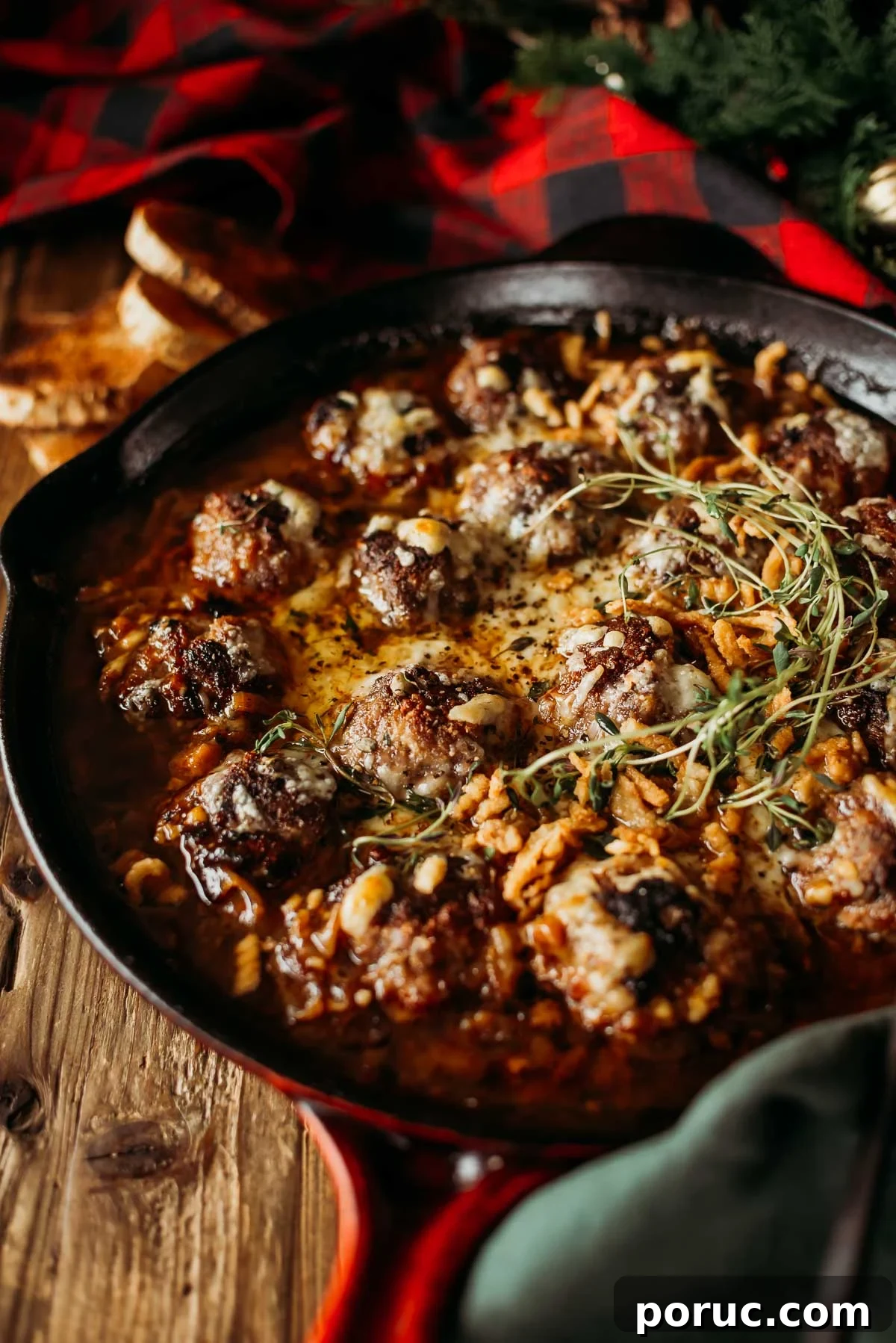 A cast iron skillet with baked french onion meatballs in sauce, garnished with herbs and crispy onions.