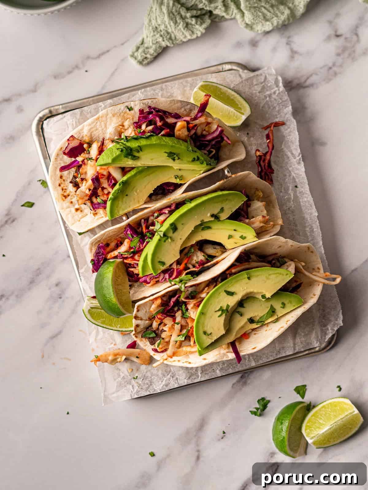 Korean BBQ Beef Tacos with Spicy Gochujang Slaw 2 A tray of tacos topped with sliced avocado and garnished with lime wedges and cilantro.
