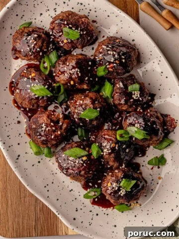 Beef meatballs topped with sesame seeds and green onions on a white plate.