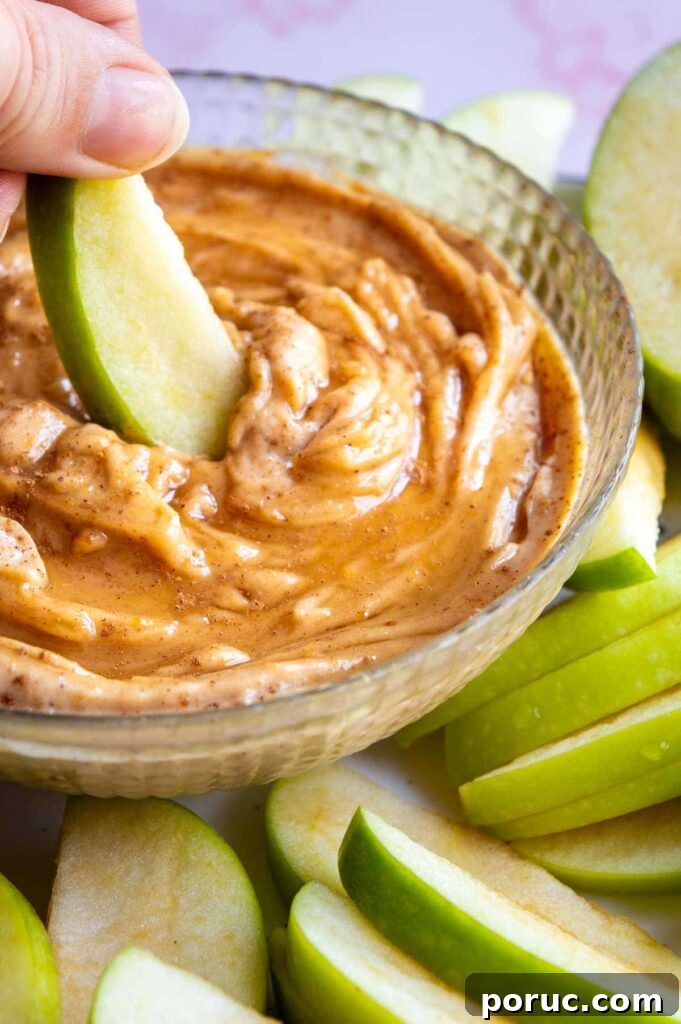 Greek Yogurt Apple Dip Recipe for Sweet & Tangy Snacks 5 A hand dipping a slice of green apple into a brown creamy dip.
