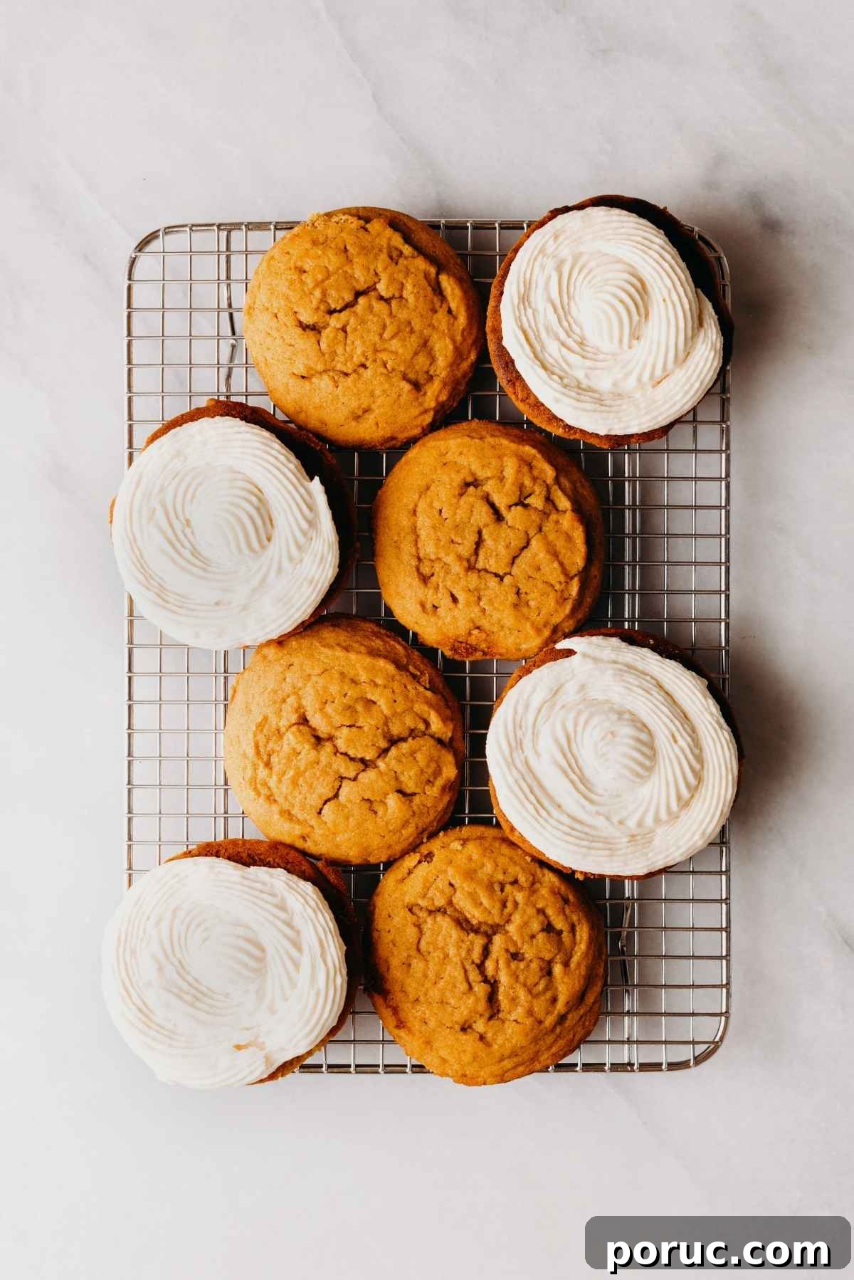 Pumpkin whoopie pies filled with maple cream cheese frosting on a wire cooling rack on a light grey marbled background.
