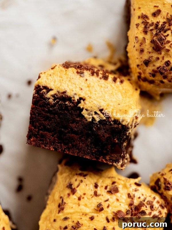 Closeup of pumpkin frosted brownie on its side on white parchment paper.