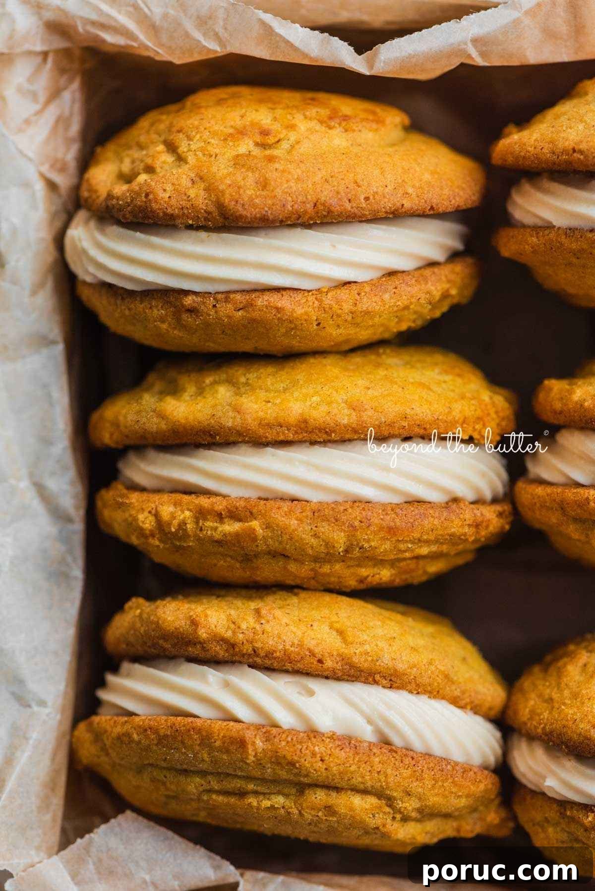 Six pumpkin whoopie pies filled with maple cream cheese frosting placed in a parchment paper lined metal baking tin.