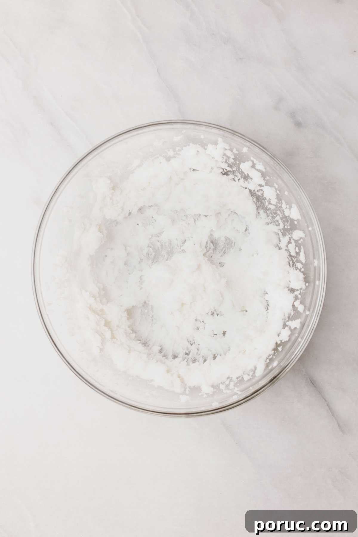 Vegetable shortening and granulated sugar beaten together in a large glass mixing bowl on a light grey marbled background.